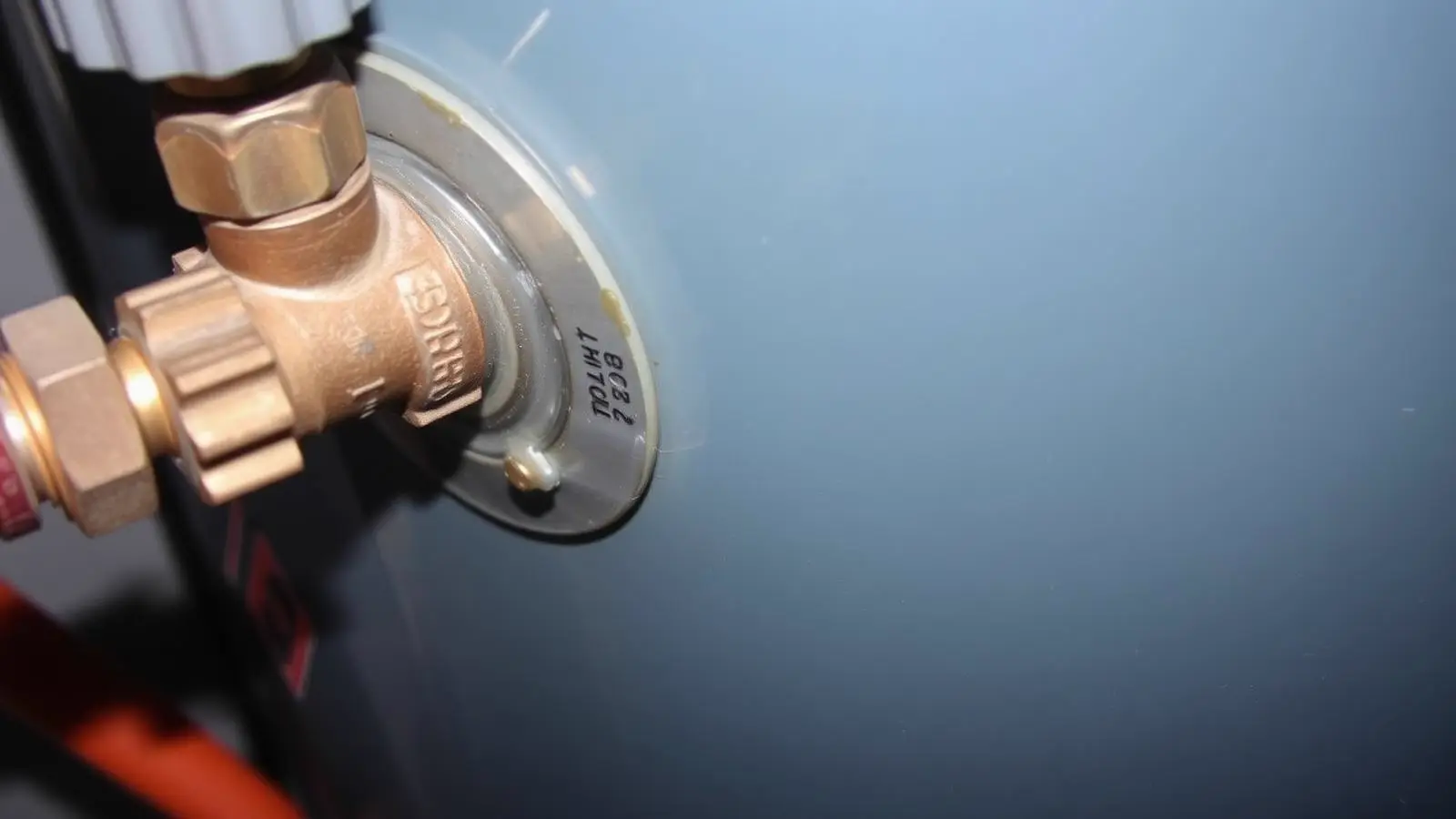 Brass pressure valve seated in the side of a water heater tank with moisture around the threads